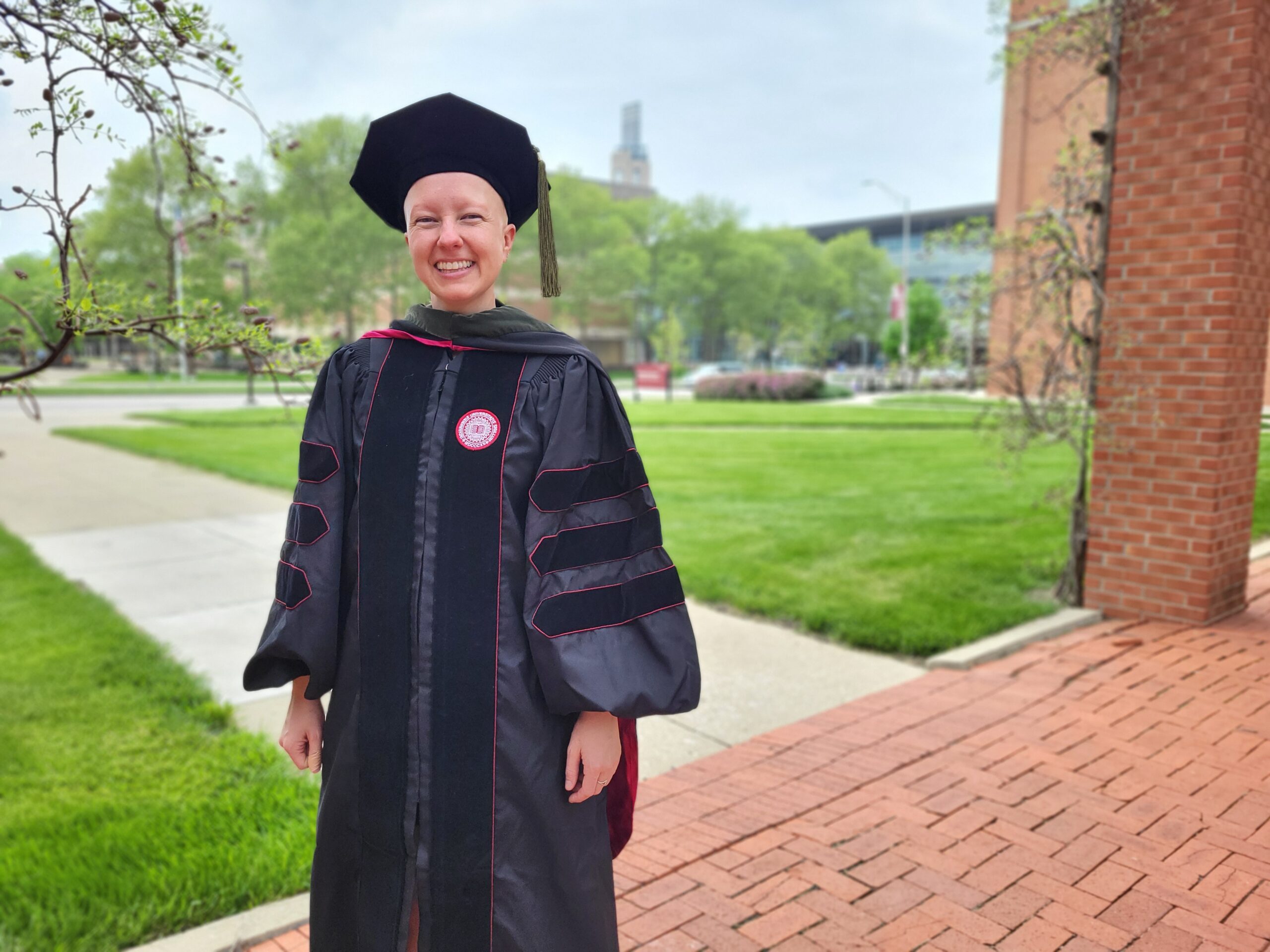 A young person wearing doctoral graduation regalia, smiling